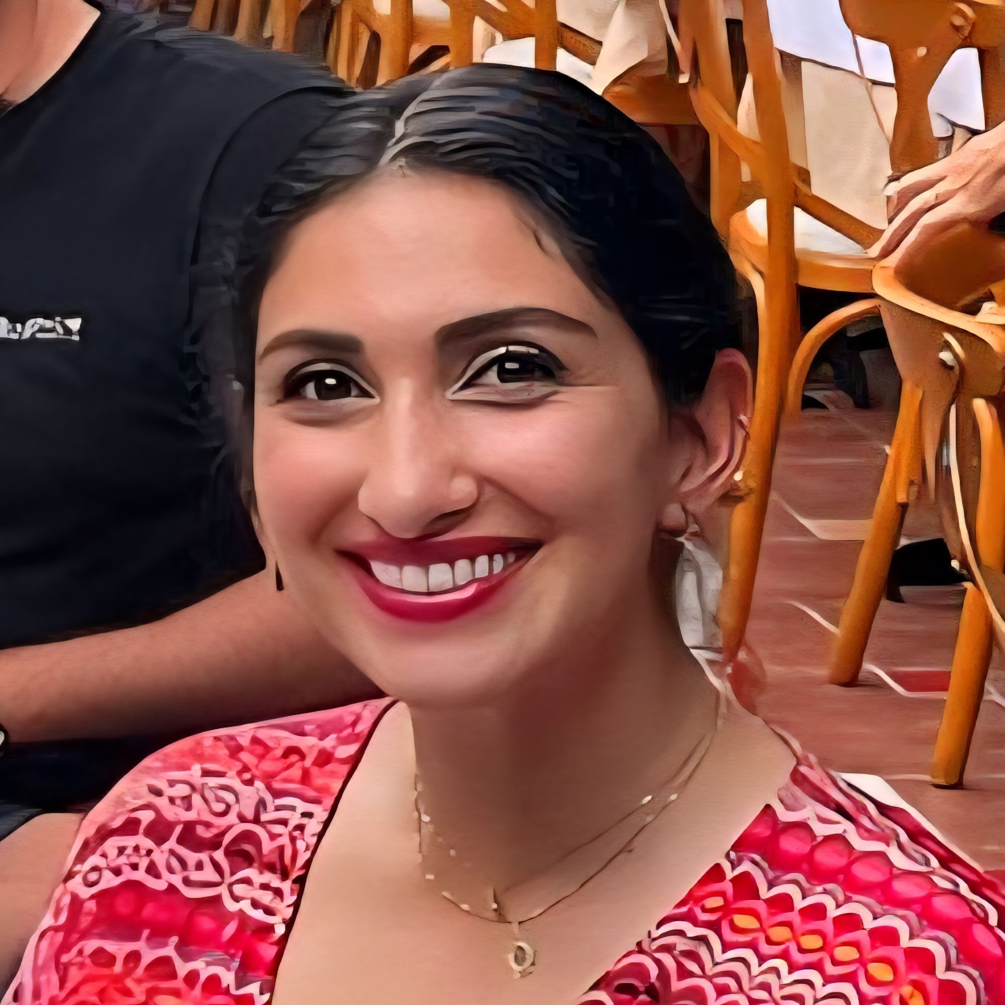 Portrait of a smiling woman with dark hair wearing a patterned red top in an outdoor setting