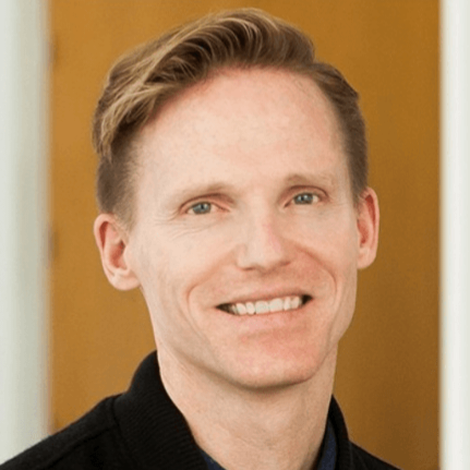 Portrait of a smiling man with blond hair wearing a dark sweater indoors