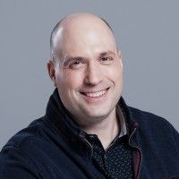 Portrait of a smiling bald man wearing a dark jacket against a neutral background