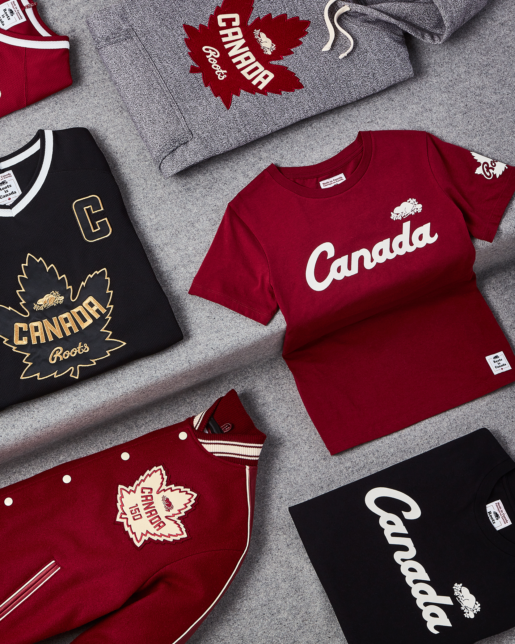 Roots Canada apparel featuring Canada and maple leaf branding arranged on a grey background.